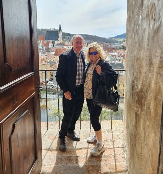 Simon and Alice standing on a balcony with old town and hills in the background